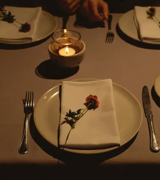 A candlelit table setting, a rose laid across a folded napkin on a plate