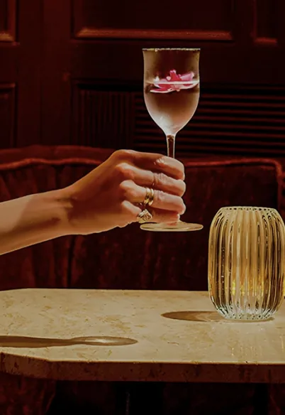 A hand lifting a glass from a marble table in a warmly lit dining room